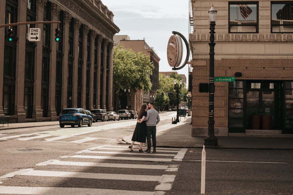 Couple walking on a sunny Downtown Portland street, featuring urban landscape for engagement photos.
