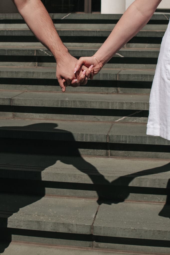 Close-up photo of a couple holding hands on Jade colored stairs, symbolizing connection in engagement photography.