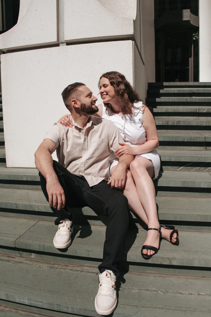 Candid engagement photo of a couple sitting intimately on jade colored urban steps.