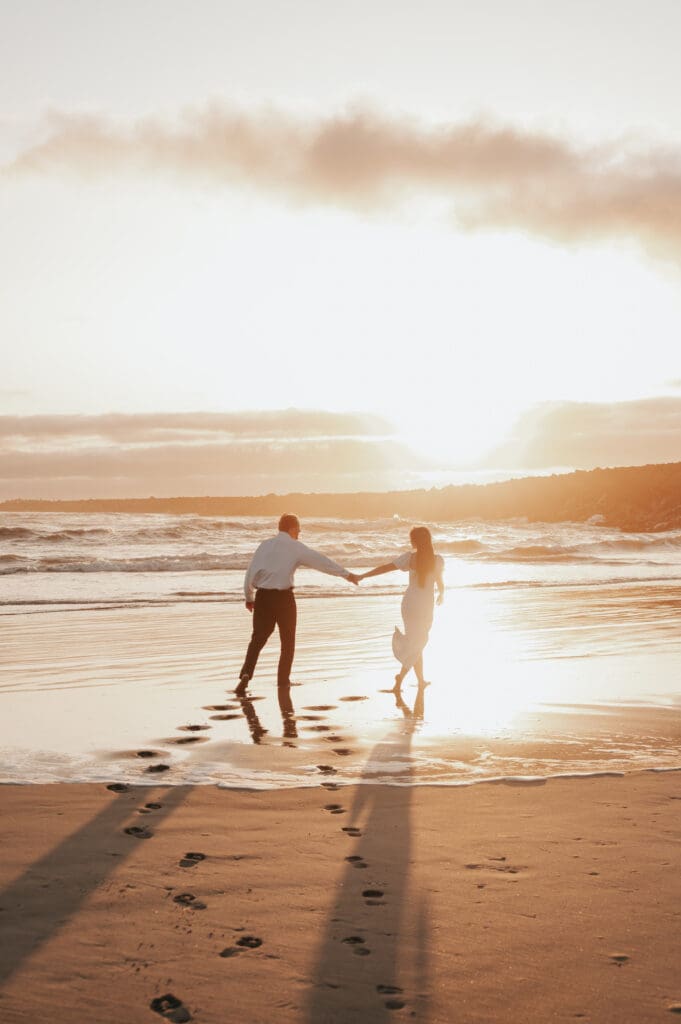Couple walks hand-in-hand along the shoreline during golden hour on the Oregon Coast