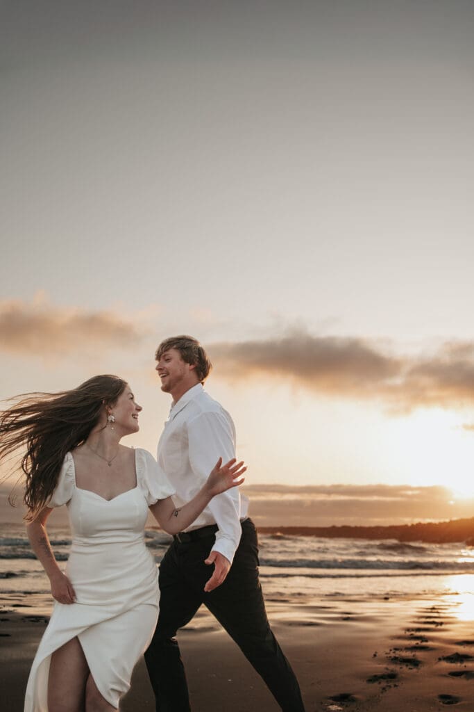 Wind-blown couple smiling at each other on Florence, Oregon coastline