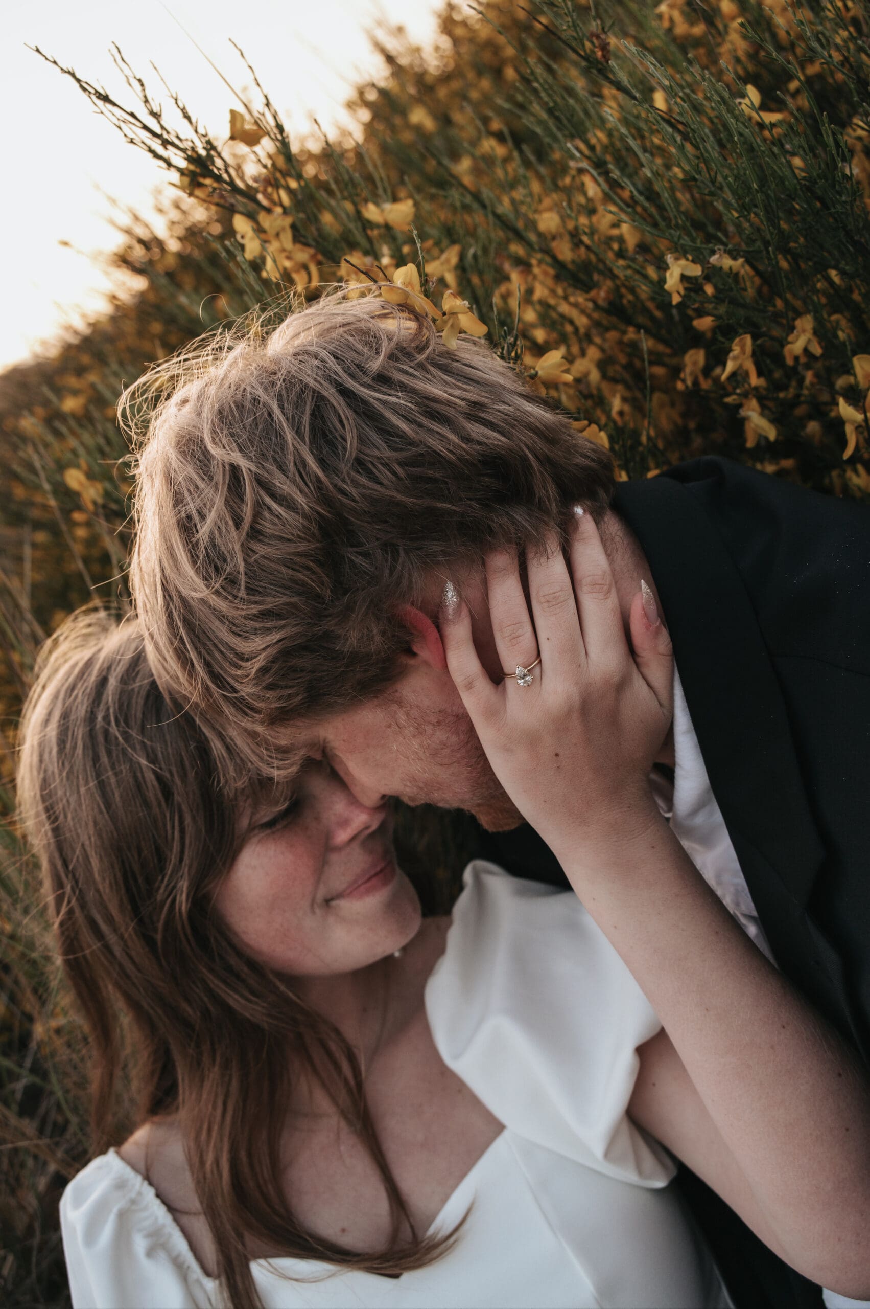 Yellow wildflowers bloom behind a couple with their foreheads together in Florence during golden hour.