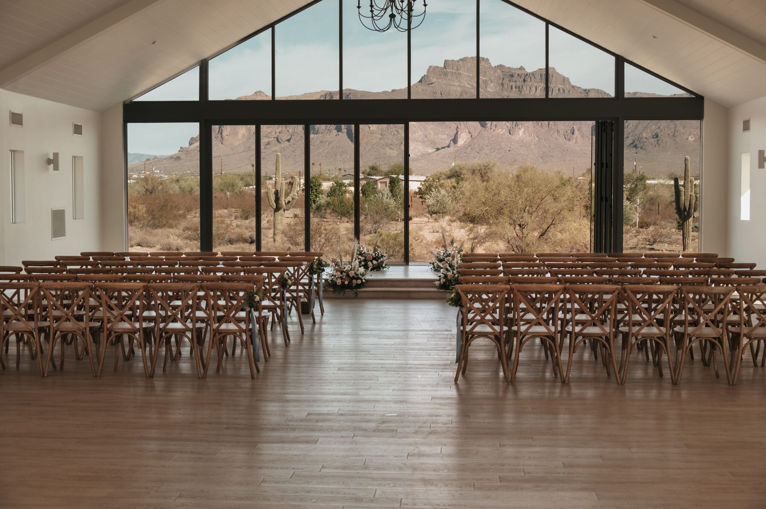 Wedding ceremony setup at Desert View with rows of wooden chairs and desert landscape seen through glass wall.