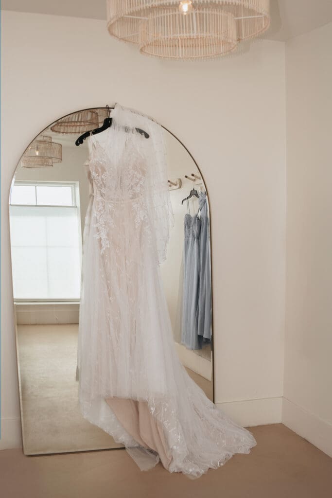 Wedding dress hanging in front of mirror in Desert View bridal suite with natural light pouring in.