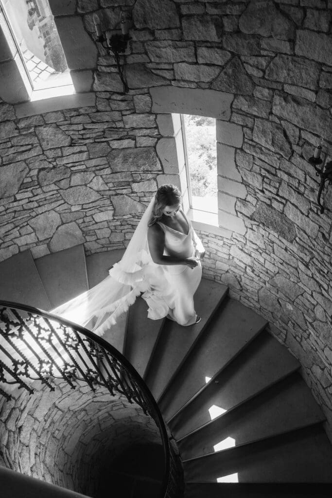 Black and white photo of bride walking down a spiral staircase at the Chateau De Lis. 