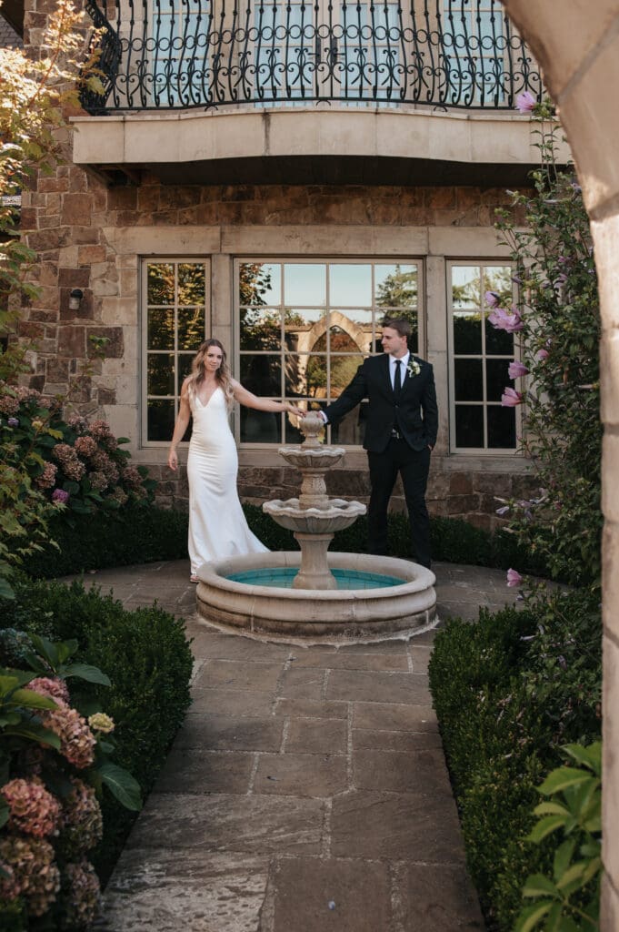 Bride and groom walking by garden fountain captured by Portland Oregon Wedding Photographer. 