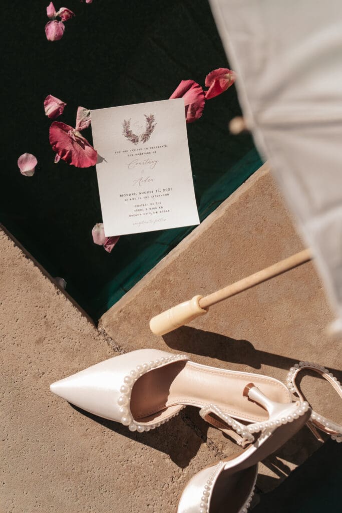 Flat lay of wedding invitation with parasol and rose petals in a pond at Portland Oregon wedding venue. 