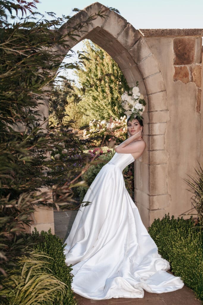 Bride leans against stone arch in fashion forward pose at garden at Chateau de Lis in Oregon City, Oregon. 