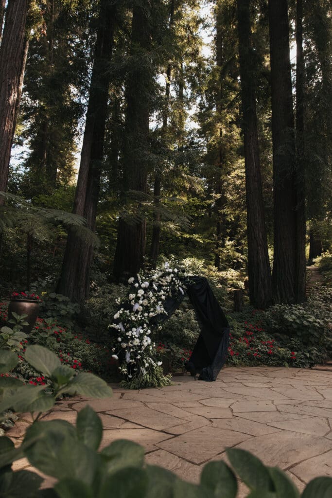 Side angle of floral wedding arbor in the ceremony space beneath the redwood trees at Nestldown.
