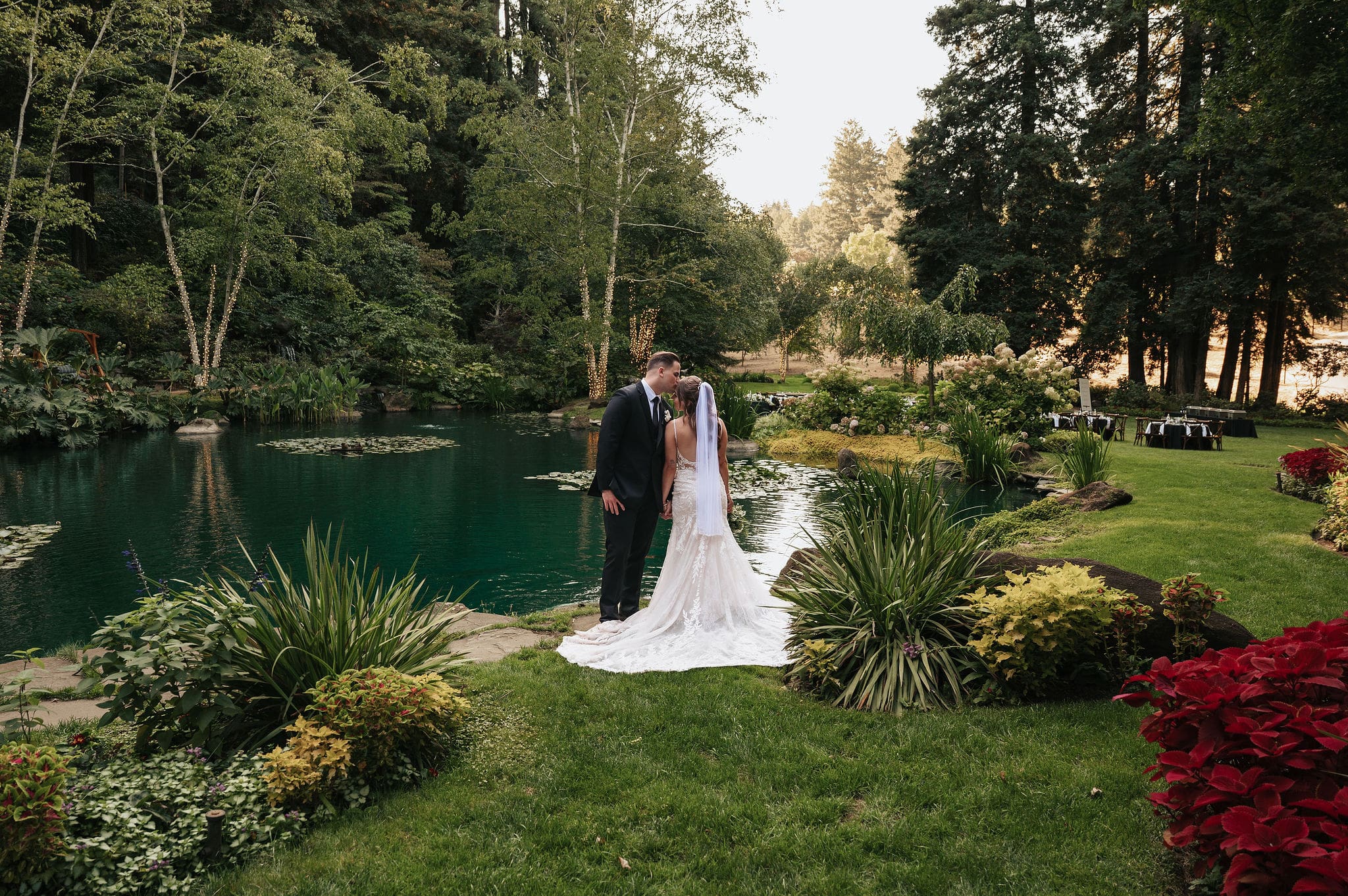 Wide shot of bride and groom kissing beside the koi pond for a portrait at the romantic Nestldown in Los Gatos, California photographed by a Nestldown wedding photographer.