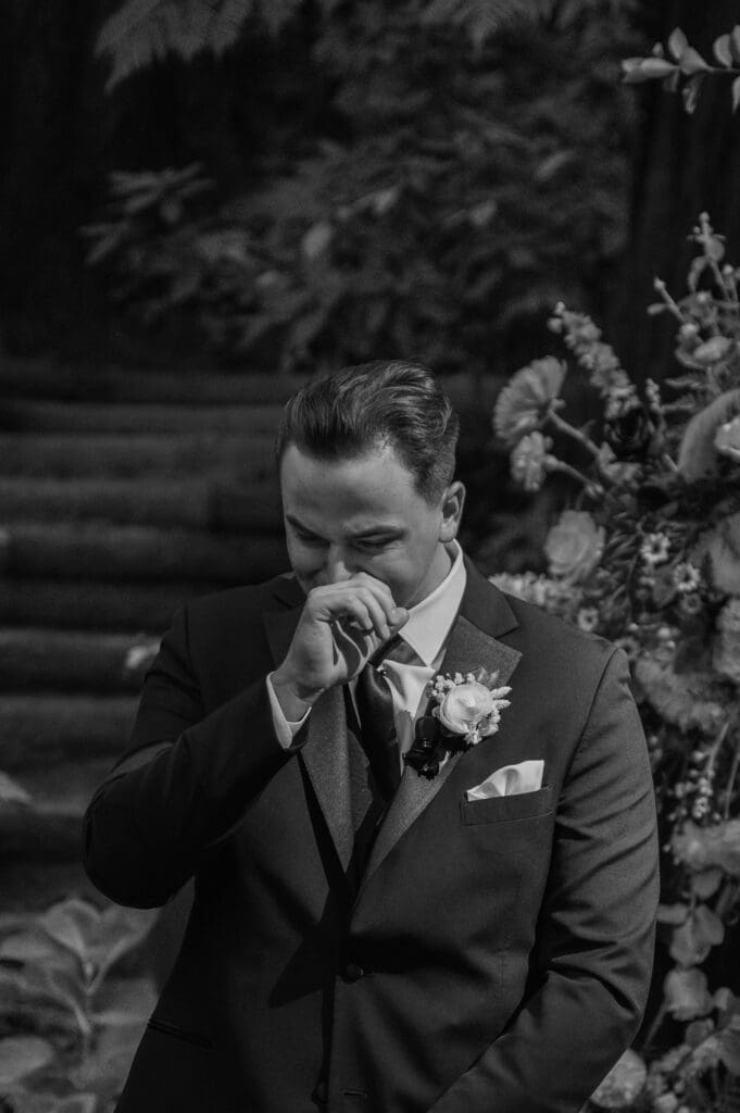 Black and white photo of groom wiping away tears during the ceremony at a heartfelt Nestldown wedding.
