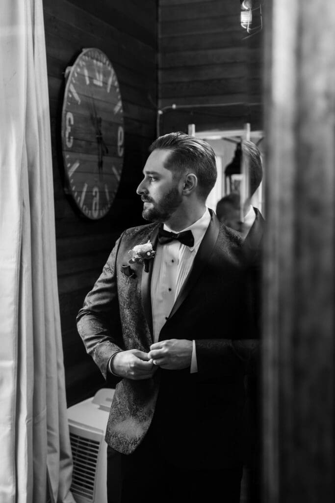 Dramatic black and white portrait of groom buttoning his jacket.