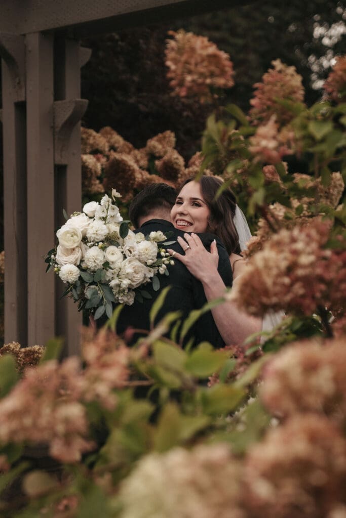 Bride and groom embrace after first look, framed by hydrangeas.