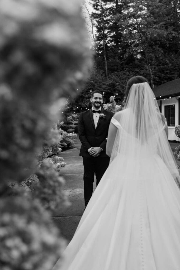 Black and white photo of groom smiling at his bride during their first look captured by Scottsdale, Arizona wedding photographer framed by hydrangeas.