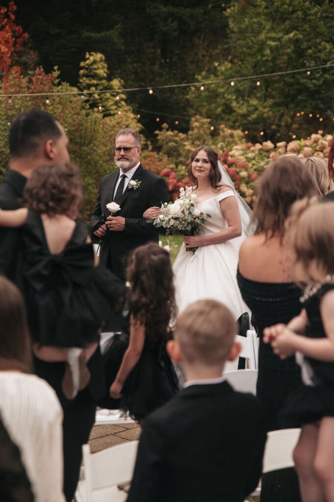Bride walking down aisle with her father surrounded by loved ones during Cape Horn Estate wedding