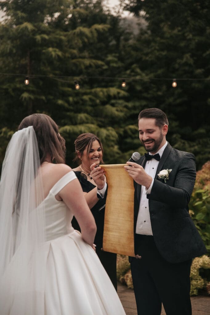 Groom smiles and reads his vows off a long scroll during wedding ceremony.