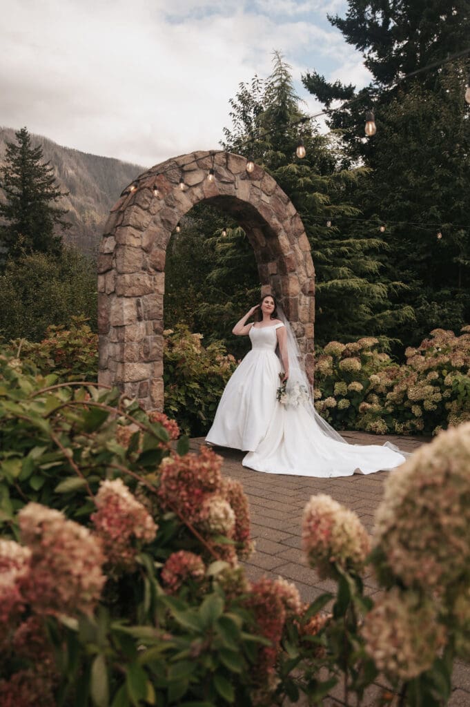 Elegant editorial bridal portrait beneath stone arch surrounded by flowers at Cape Horn Estate.