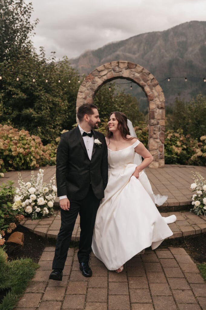 Bride and groom walking in front of stone archway during Cape Horn Estate wedding