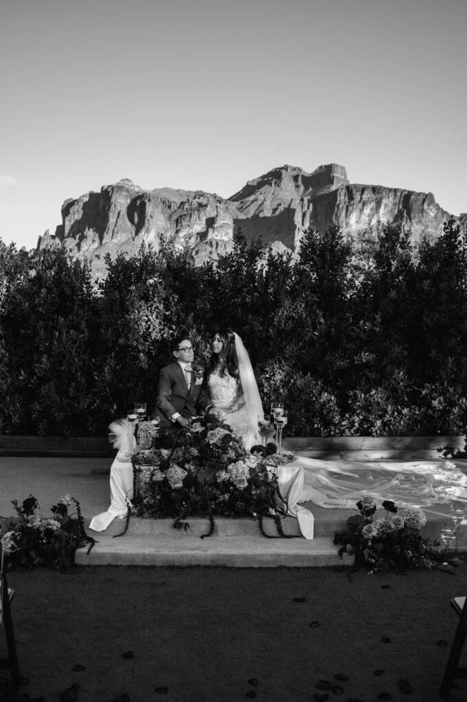 Black and white wedding portrait of Bride and Groom sitting at the alter at The Paseo Venue with Superstition Mountain views in the background.
