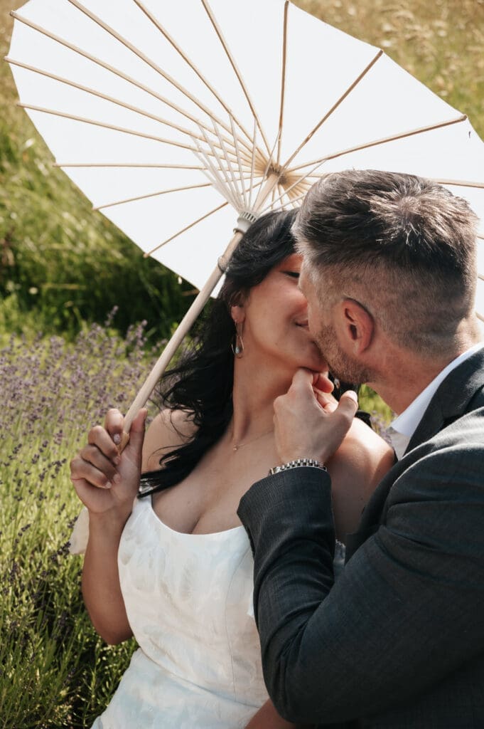 Couple sharing an intimate moment under a parasol in front of the lavender at Villa Catalana Cellars.