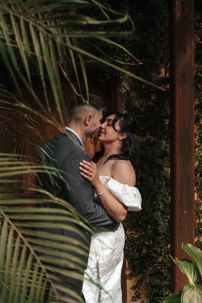 Romantic portrait of newlyweds embracing beside a rustic doorway at Villa Catalana Cellars.