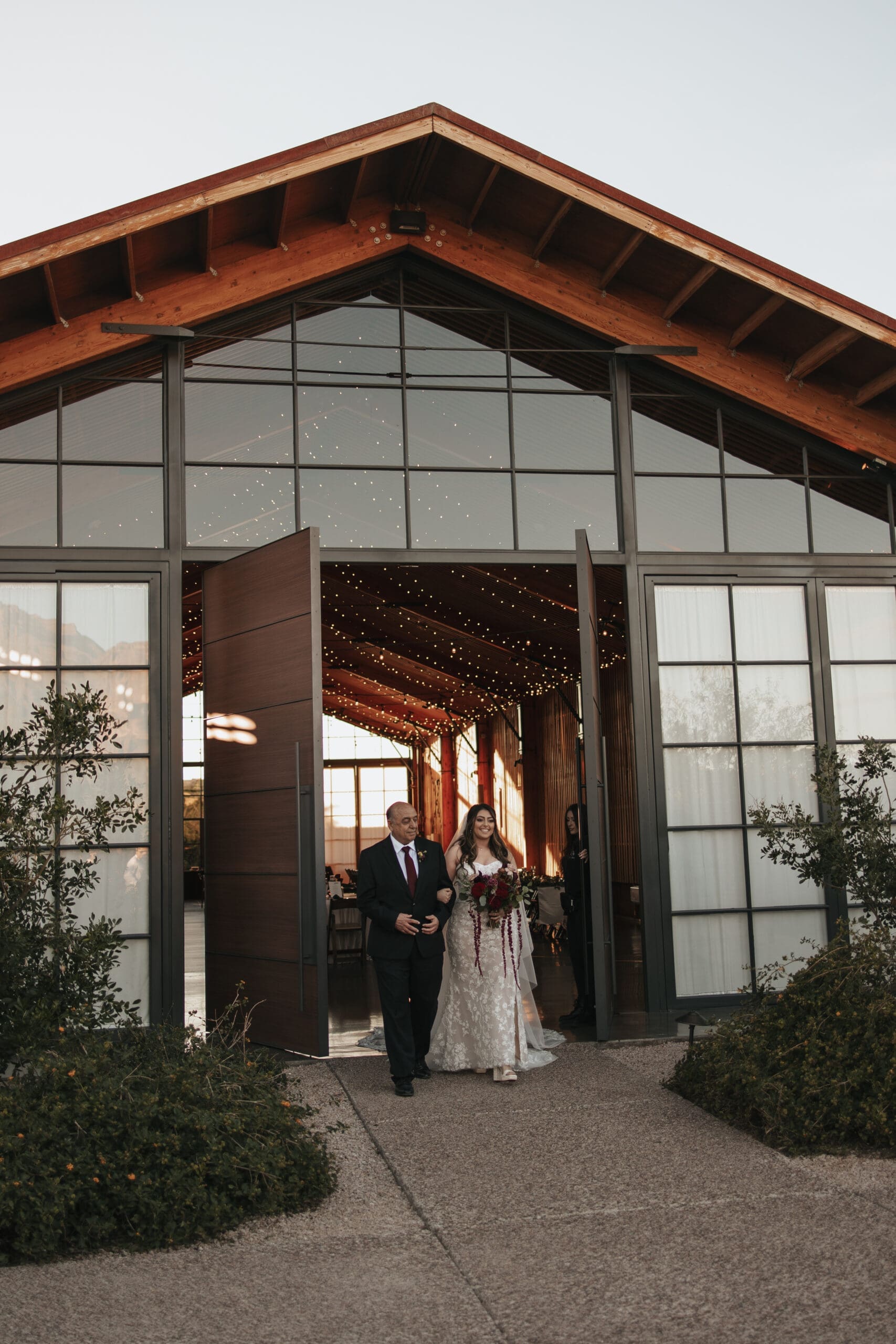 Bride walks out of building with her father during her wedding at the luxury, Award-Winning Paseo Venue in Apache Junction, AZ.